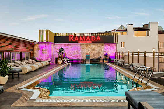 Bilde av et utendørs basseng med solsenger rundt og et skilt med teksten Ramada by Wyndham. (AI-generert tekst)