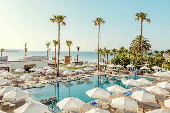 Utendørs bassengområde med solsenger og parasoller, omgitt av palmer og nær sjøen. (AI-generert tekst)