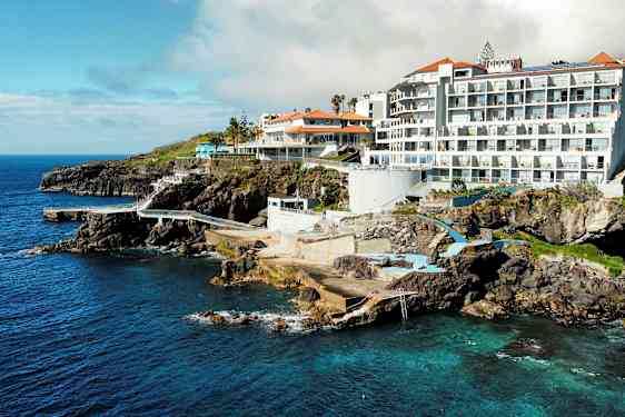 Hotellbygninger ved klipper med utsikt over havet og bassengområder. (AI-generert tekst)