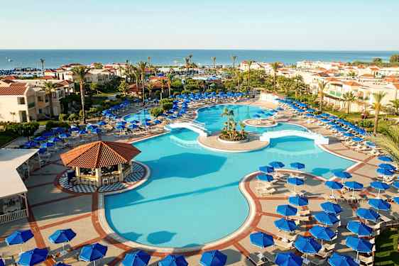 Utendørs basseng omgitt av solsenger og parasoller, med hotellbygninger i bakgrunnen mot havet. (AI-generert tekst)