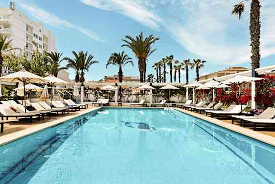 Et utendørsbasseng omgitt av solsenger og parasoller med palmer i bakgrunnen. (AI-generert tekst)