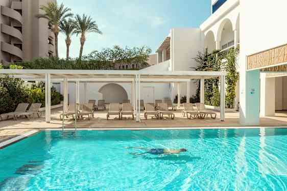 Et utendørs svømmebasseng med solsenger ved siden av og en person som svømmer i vannet. (AI-generert tekst)