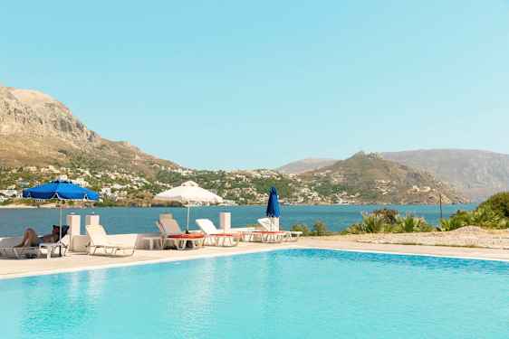 Utendørsbasseng med solsenger og parasoller, samt utsikt over havet og fjellene. (AI-generert tekst)