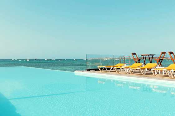 Svømmebasseng med utsikt over havet og solsenger ved siden. (AI-generert tekst)