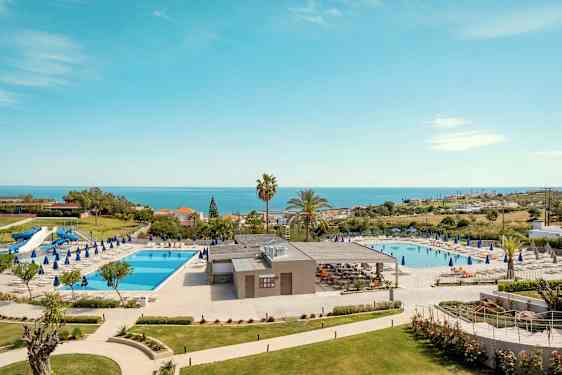 Hotellområde med to svømmebassenger, solsenger og havutsikt. (AI-generert tekst)