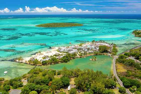 Flyfoto av en strandresort omgitt av turkisblått vann og grøntområder. (AI-generert tekst)