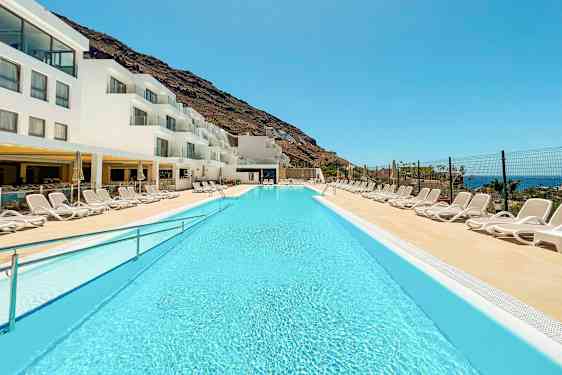 Et basseng ved et hotell med hvite bygninger og solsenger. (AI-generert tekst)