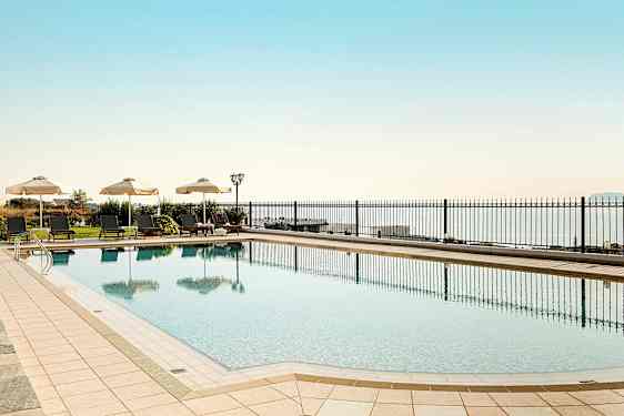 Et utendørs svømmebasseng med solsenger og parasoller ved siden av, med havet i bakgrunnen. (AI-generert tekst)