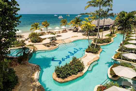 Bassengområde ved stranden med palmer og parasoller. (AI-generert tekst)