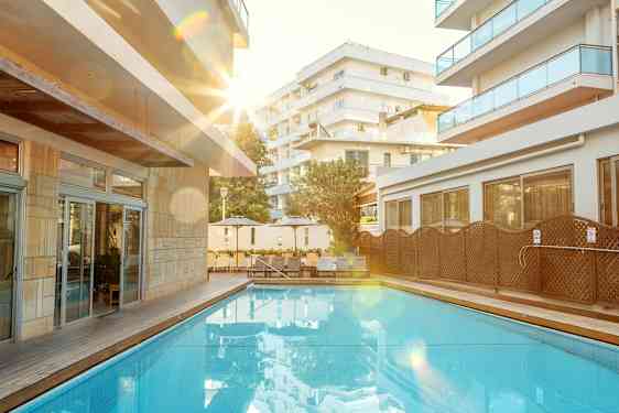 Utendørs svømmebasseng med omkringliggende solsenger og bygninger. (AI-generert tekst)