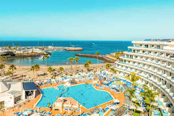 Bilde av et hotell med bassengområde, strand og havneinnløp ved sjøen. (AI-generert tekst)