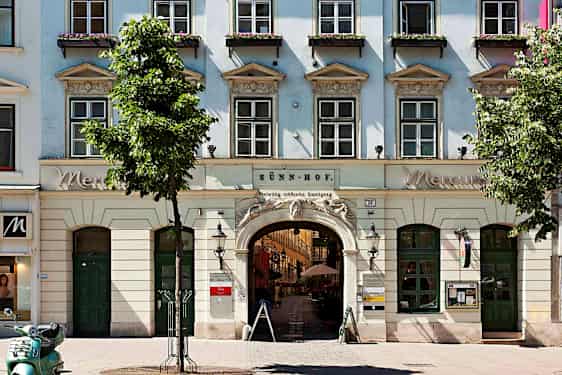 En bygning med vinduer, buede innganger og blomsterkasser på vinduskarmene. (AI-generert tekst)