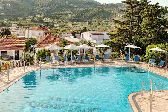 Utendørsbasseng med solsenger og parasoller ved et hotell, omgitt av trær og bygninger. (AI-generert tekst)