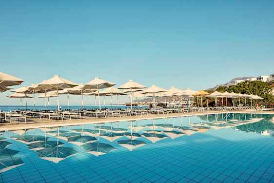 Solstoler og parasoller ved et basseng med utsikt over havet. (AI-generert tekst)