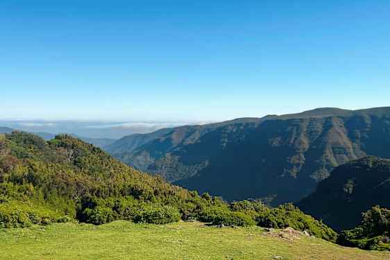 Bildet viser et landskap med frodige åser og fjell under en klar blå himmel. (AI-generert tekst)