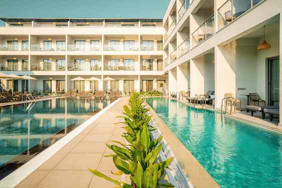 Bilde av hotell med basseng foran bygningen med solsenger og grønne planter. (AI-generert tekst)