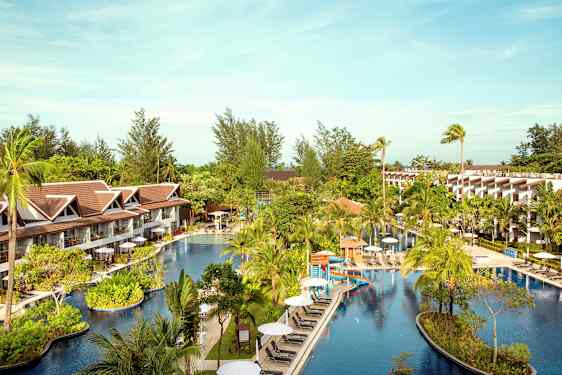 Hotellområde med et stort basseng omgitt av palmer og bygninger. (AI-generert tekst)