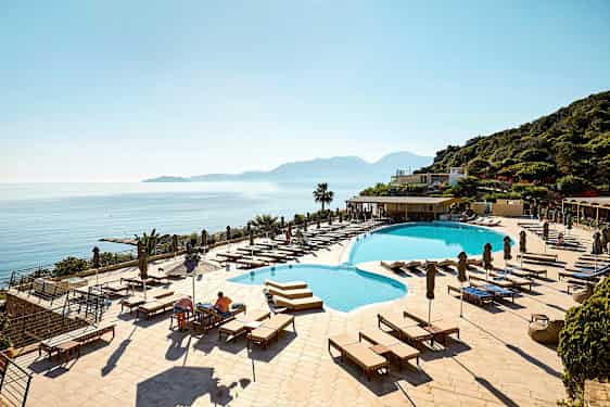 Hotellbasseng med solsenger og utsikt over havet og fjell. (AI-generert tekst)
