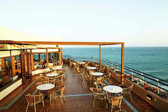 En terrasse med bord og stoler og utsikt over havet. (AI-generert tekst)