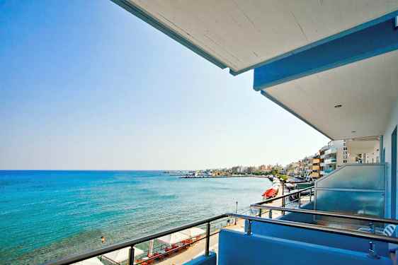 Utsikt fra en balkong mot sjøen og en strandpromenade. (AI-generert tekst)