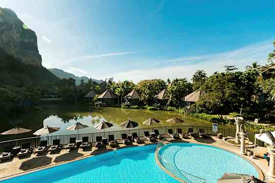 En idyllisk ferieanlegg med bungalower ved en fredelig dam og et basseng med solsenger i forgrunnen. (AI-generert tekst)