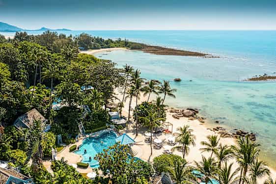 Et tropisk landskap med en strand omgitt av palmetrær og klart blått vann. Det er et basseng og grønne områder i forgrunnen. (AI-generert tekst)