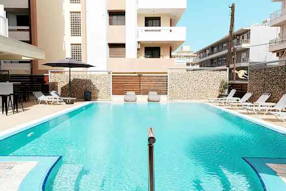 Et utendørs basseng omgitt av solsenger og bygninger. (AI-generert tekst)