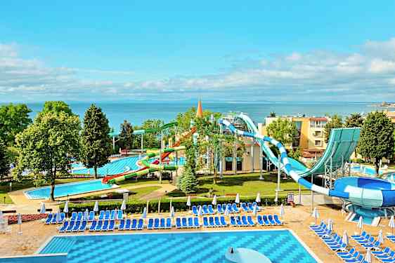 En vannpark ved sjøen med vannsklier og bassenger omgitt av solsenger og parasoller. (AI-generert tekst)