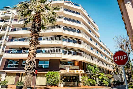 Et hotell med flere etasjer og et palmetre foran. Skiltet "STOP" er synlig til høyre. (AI-generert tekst)