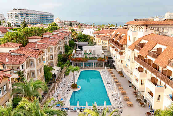 Hotellområde med et basseng omgitt av solsenger og bygninger med røde tak. (AI-generert tekst)