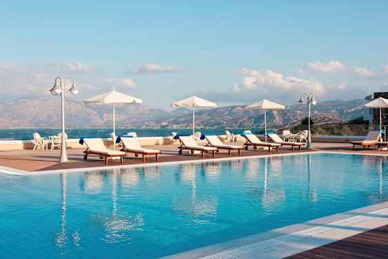Solstoler og parasoller ved et utendørsbasseng med utsikt mot fjell og hav. (AI-generert tekst)