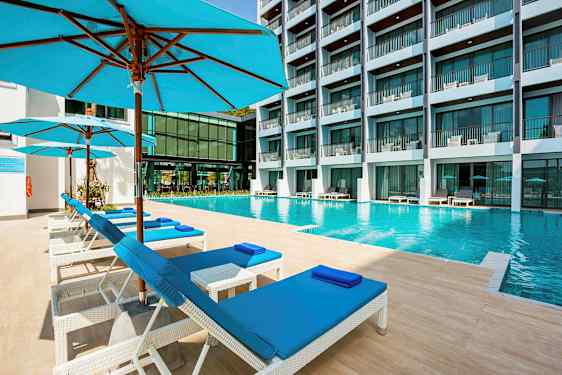Et svømmebasseng på et hotell med solsenger og parasoller i forgrunnen. (AI-generert tekst)