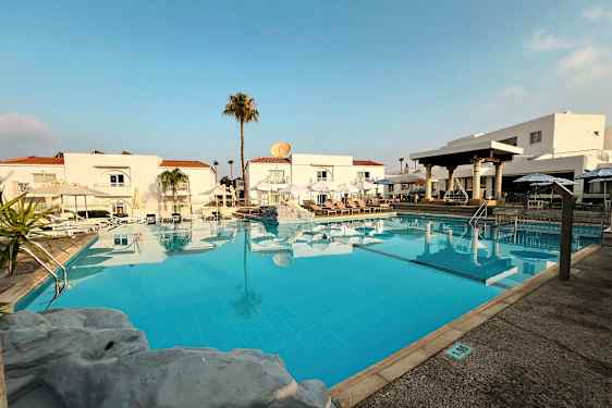 Et utendørs basseng foran hvite bygninger med røde tak. (AI-generert tekst)