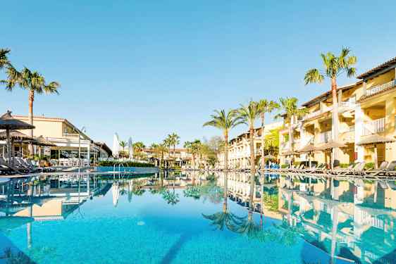 Hotellbygninger og svømmebasseng med solsenger ved bassengkanten. (AI-generert tekst)