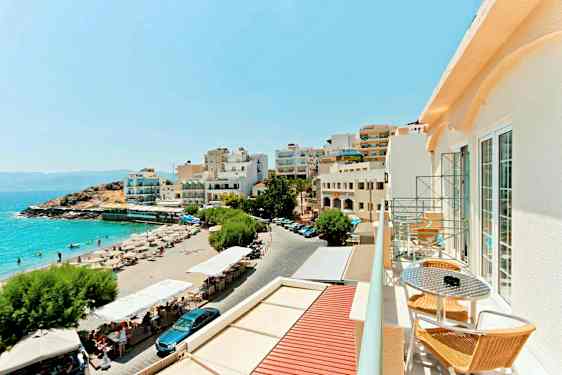 Utsikt over en sandstrand med solsenger og parasoller ved siden av bygninger med utsikt over havet. (AI-generert tekst)