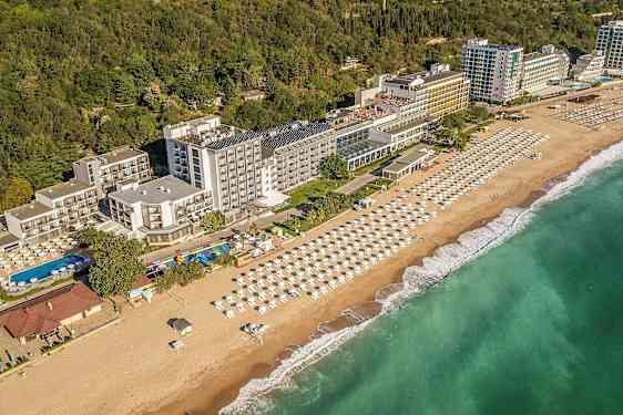 Utsikt over hotell ved kysten, med strand og parasoller samt grøntområder i bakgrunnen. (AI-generert tekst)