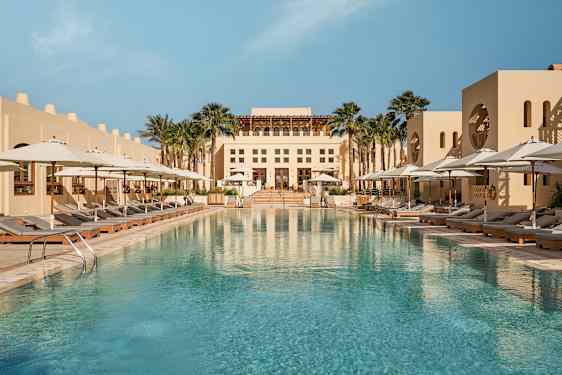 Et stort utendørsbasseng omgitt av solsenger med hvite parasoller og en bygning i bakgrunnen. (AI-generert tekst)