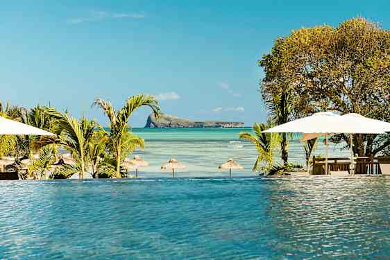 Et infinitybasseng med utsikt over en strand med parasoller og en liten øy i havet. (AI-generert tekst)