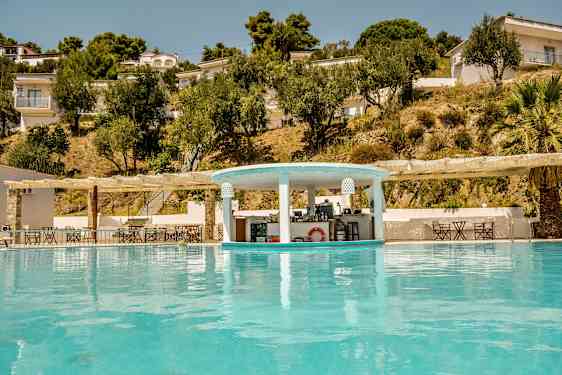 Et basseng med en bassengbar og omkringliggende bygninger og trær på skråningen. (AI-generert tekst)