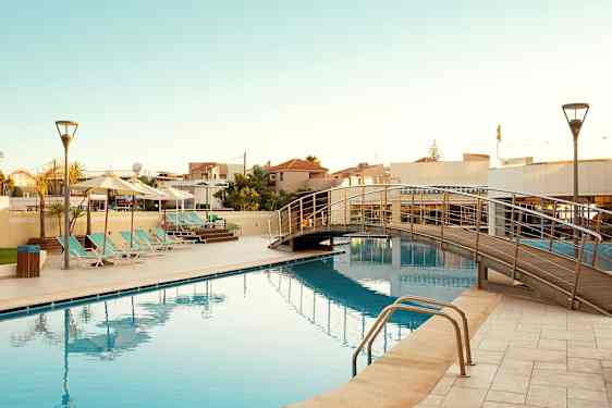 Et utendørs basseng med solsenger og en gangbro over vannet. (AI-generert tekst)