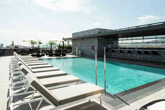 Bilde av en solfylt takterrasse med et basseng omgitt av solsenger og parasoller. (AI-generert tekst)