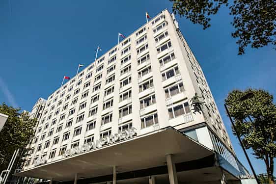 Leilighetsbygg med synlige vinduer og flagg på taket. (AI-generert tekst)