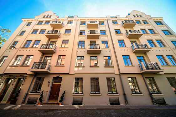 Fasade av en beige bygning med flere balkonger og blå vinduer. (AI-generert tekst)