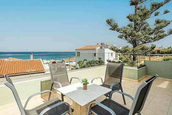 En terrasse med stoler og bord samt utsikt over havet og omkringliggende hus. (AI-generert tekst)