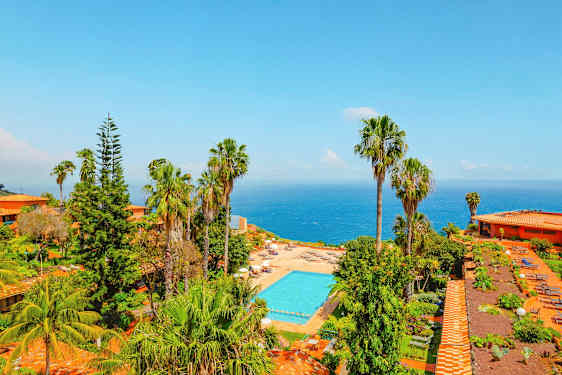 Utsikt over et bassengområde omgitt av frodighet og palmer, med havet i bakgrunnen. (AI-generert tekst)