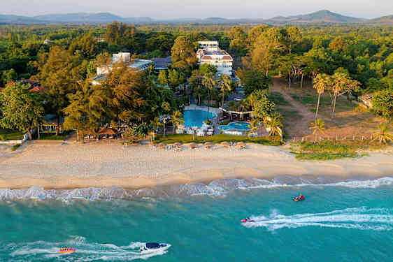 En strand med parasoller og stoler samt et hotellkompleks og bassenger i bakgrunnen omgitt av vegetasjon. (AI-generert tekst)