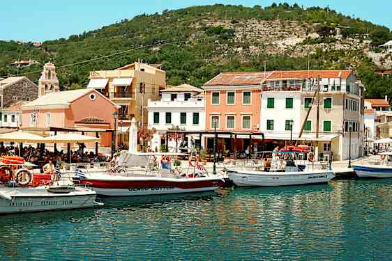 En havn med flere båter foran fargerike bygninger og omgitt av åser. (AI-generert tekst)