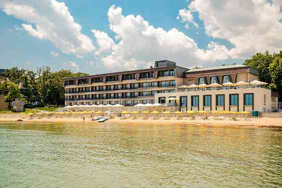 Fleretasjes hotell ved stranden med gule parasoller og klar blå himmel. (AI-generert tekst)