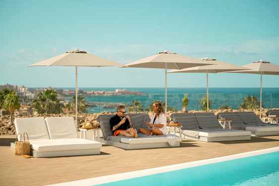 Solstoler og parasoller ved et basseng med utsikt over havet. (AI-generert tekst)