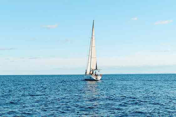 En seilbåt seiler på et åpent hav under en klar himmel. (AI-generert tekst)